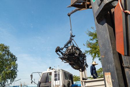 A forklift and workers are lifting an old car's engine for recycling.