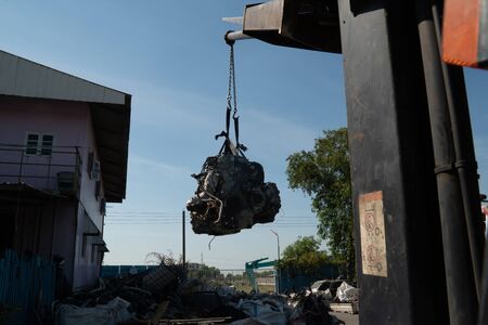 A forklift and workers are lifting an old car's engine for recycling.の写真素材
