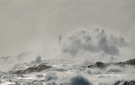Rough sea, big wave when breaking on the coast and silhouette of lighthouse in background, Telde,...