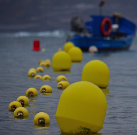 Line of buoys in foreground, calm sea and fishing boat out of focus in backgroundの写真素材