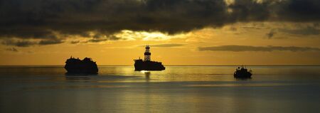 Sunrise from the bay with anchored ships, calm sea and cloudy skyの写真素材