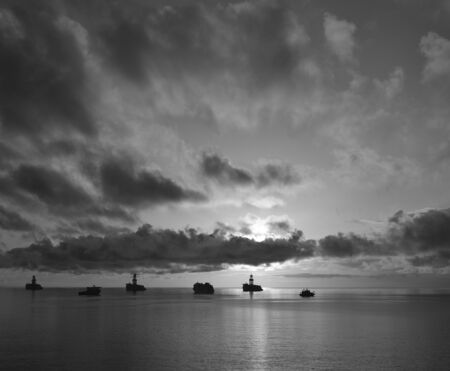 Intense sunrise with awesome sky of scattered clouds, calm sea and ships in the bay, monochrome effectの写真素材