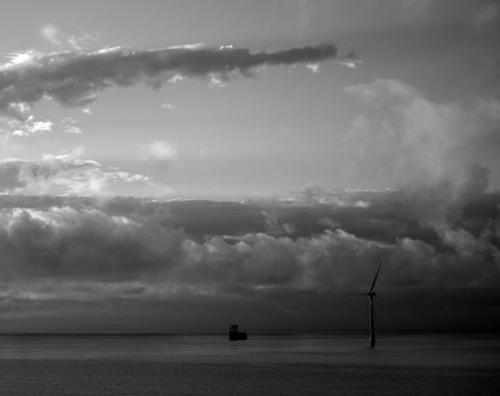 Dawn on the sea with cloudy sky and marine wind turbine, black and white