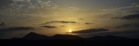 Sunset behind the mountains and sky with scattered clouds, view from Famara, Lanzarote, Spain