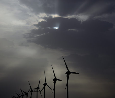 Dawn with sun rays through the clouds and backlit wind turbines