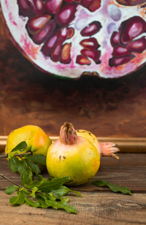 Image of whole scarred unripe pomegranates with a blurred painting background on rustic tableの写真素材