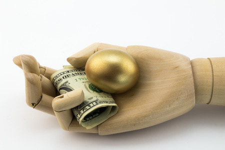 Golden nest egg in palm of wooden hand with dollar notesの写真素材