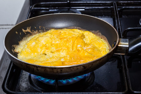 Scrambled eggs cooking in pan on gas flame close up