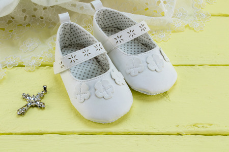 Pair of white baby booties on yellow table with lace dressの写真素材