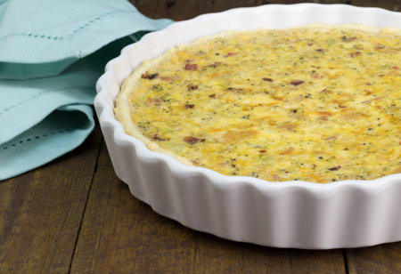 Quiche with cheese, bacon and mushroom on rustic wooden table - Open pie in white dish with...