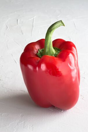 Red bell pepper isolated on stucco textured white surface with space for text - Vertical image  Paprika pepper backgroundの写真素材