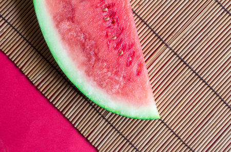 Watermelon slice on reed tablemat with red background close up
