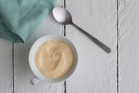 Yogurt in cup on white rustic wooden table background with silver spoon - Top view photographの写真素材