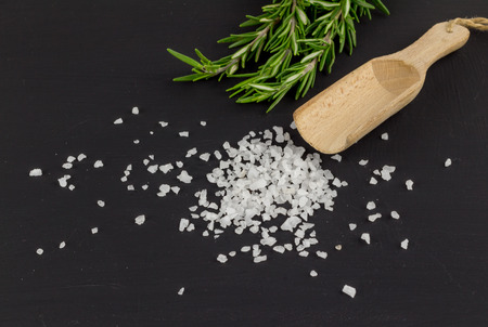 Salt heap on rustic black background with rosemary herb and wooden spoonの写真素材