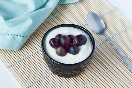 Yoghurt cup with black grapes and spoon close upの写真素材