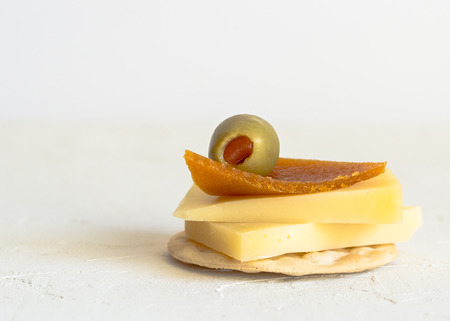 Cheese on cracker with pimento stuffed green olive and dried peach roll decoration isolated on whiteの写真素材