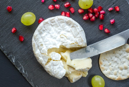 Camembert cheese, knife, cracker and pomegranate seeds on cheese slate board