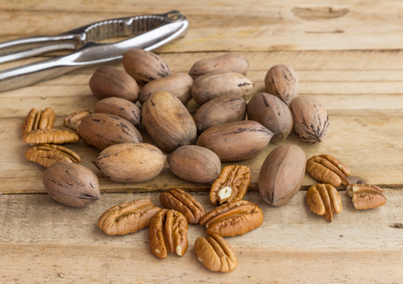 Pecan nuts on rustic wooden table, whole and peeled with nut cracker in background - selective focus imageの写真素材
