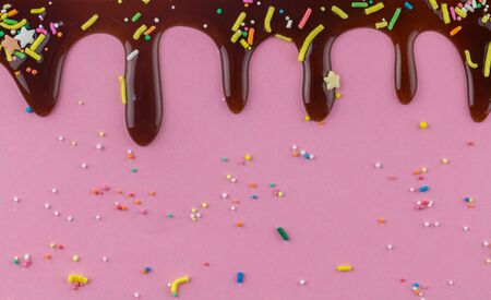 Chocolate cake topping sprinkles with chocolate flowing down on pink backgroundの写真素材