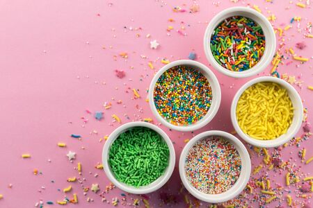 Sprinkles on pink background - Assorted colourful cake topping sprinkles in little white bowls on pink on bottom corner with space for text - top viewの写真素材