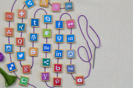 QUEENSTOWN, SOUTH AFRICA - 7 JULY 2019 -Social media background with social media logos on wooden game blocks joined with embroidery thread and needle on white linen background - Conceptのeditorial素材