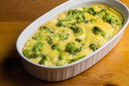 Broccoli egg and cheese baked casserole dish on brown wooden table - side view with selective focusの写真素材