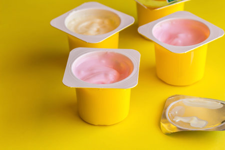 Fruit flavoured yogurt in yellow plastic cups on bright yellow background with silver foil lid - Yoghurt cup background with selective focusの写真素材