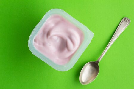 Strawberry yogurt cup on bright green background with small silver spoon - top viewの写真素材