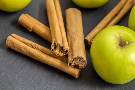 Cinnamon sticks and green apples isolated on black slate background with selective focus - close up horizontal imageの写真素材