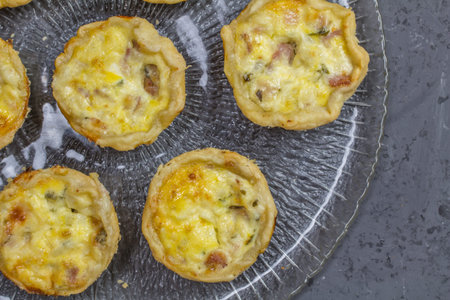 Mini quiche photo - many small savory tartlets on glass serving plate - top view