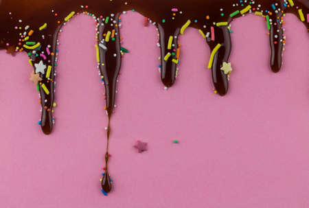 Chocolate dripping on pink background with dots, sprinkles and fun stars - copy space for birthday invitation cardの写真素材