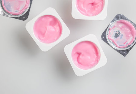Pink yogurt cup - top view of strawberry yoghurt in plastic cups with foil lids on white background...