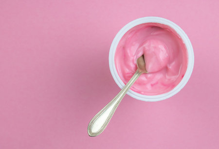 Strawberry pink yogurt in small plastic cup with little spoon isolated on pink background with copy spaceの写真素材