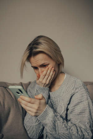 Ukrainian frightened woman reads war news on her phone. The woman is afraid of the sounds of air raids and explosions. The concept of fear. stop the war. Pray for Ukraine. we are available to Ukraine.の写真素材