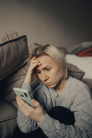Ukrainian frightened woman reads war news on her phone. The woman is afraid of the sounds of air raids and explosions. The concept of fear. Stop the war. Pray for Ukraine. we are available to Ukraine.の写真素材