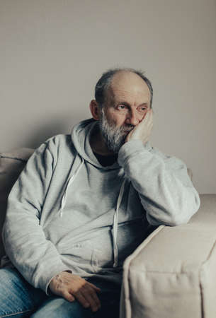Ukrainian gray haired man thought about the war. A middle aged man sits on a couch and looks thoughtfully to the side.の写真素材