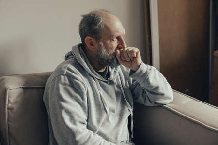 Ukrainian gray haired man thought about the war. A middle aged man sits on a couch and looks thoughtfully to the side.の写真素材