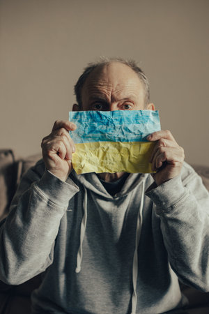 Ukrainian frightened gray haired middle aged man holds the flag of Ukraine in front of him. Portrait...