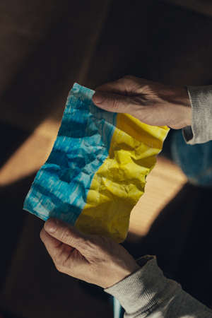Crumpled flag of Ukraine. A middle aged man holds a crumpled flag of Ukraine in his hands. stop war. Pray for Ukraine. We support Ukraine.の写真素材