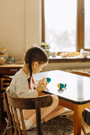 Ukrainian girl paints the egg blue and yellow. The child loves and supports his country. Cute little child girl painting with blue and yellow colors Easter eggs. Hands of a girl with a easter egg.の写真素材