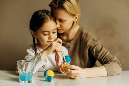 Portrait of a mother and daughter painting an egg in blue and yellow. Ukrainian family is preparing for Easter. The egg is painted in the color of the flag of Ukraine.の写真素材
