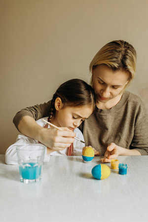 Portrait of a mother and daughter painting an egg in blue and yellow. Ukrainian family is preparing...