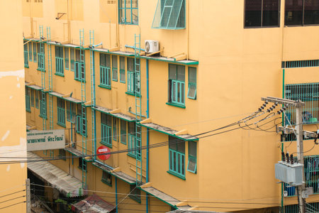 Behind of the yellow building with green windows and tranformer beside in the middle market of...
