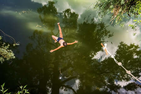 A boy jumps in a lake with a rope from a tree