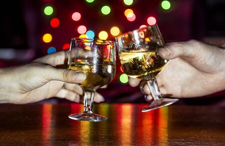 Hands with glasses of sparkling wine against the backdrop of a colorful Bokehの写真素材