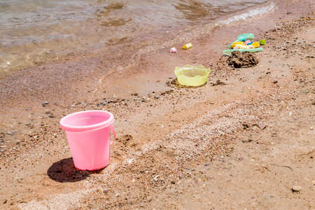 Colorful children's toys scattered on the sand at the beach in sunny dayの写真素材