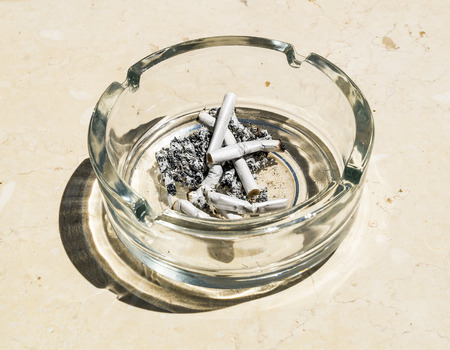 Cigarette butts from ash in the glass ashtray on a stone table topの写真素材