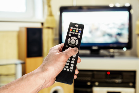 Men's hand sends the remote control on the TV in the living roomの写真素材