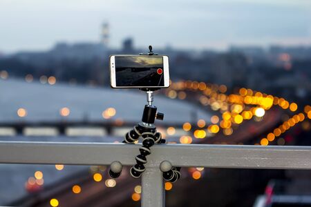 The smartphone is fixed on a tripod shooting a video with a colorful panorama of the cityの写真素材