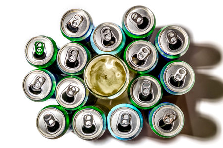 Used aluminum cans of beer and a glass of beer stand in rows on a light background